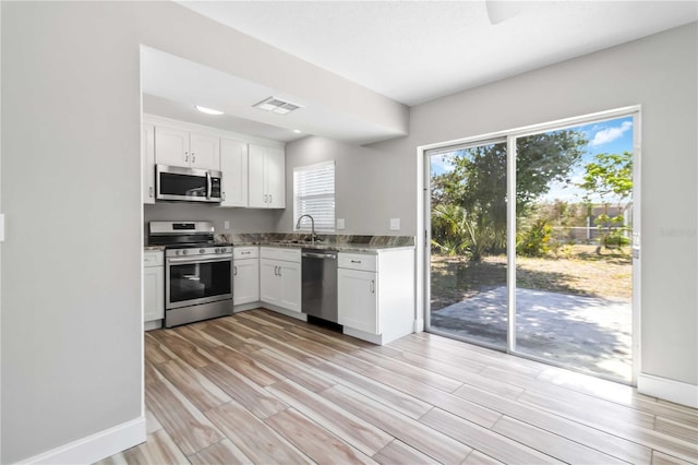 kitchen with stone countertops, light hardwood / wood-style flooring, stainless steel appliances, sink, and white cabinetry