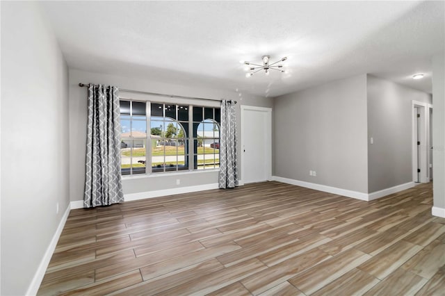 unfurnished room featuring a textured ceiling, light hardwood / wood-style flooring, and an inviting chandelier