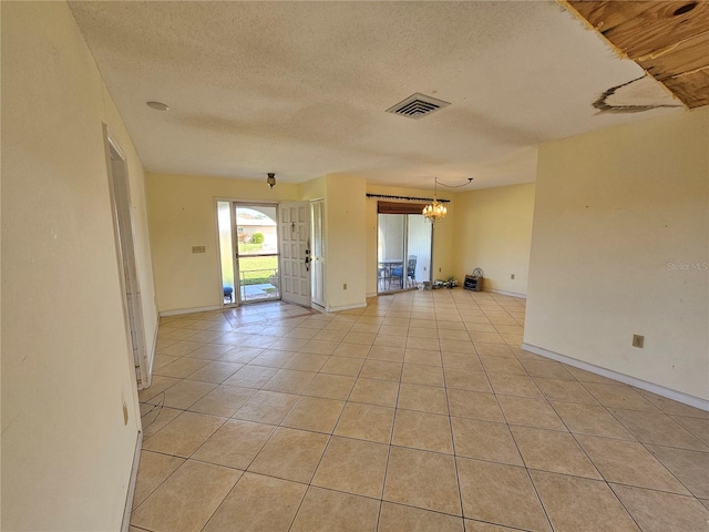 tiled empty room featuring a textured ceiling and an inviting chandelier