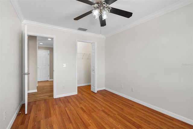 unfurnished bedroom with light hardwood / wood-style flooring, a spacious closet, crown molding, and ceiling fan