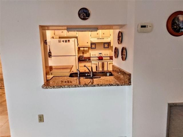 kitchen featuring dark stone countertops, white appliances, sink, and light tile patterned floors