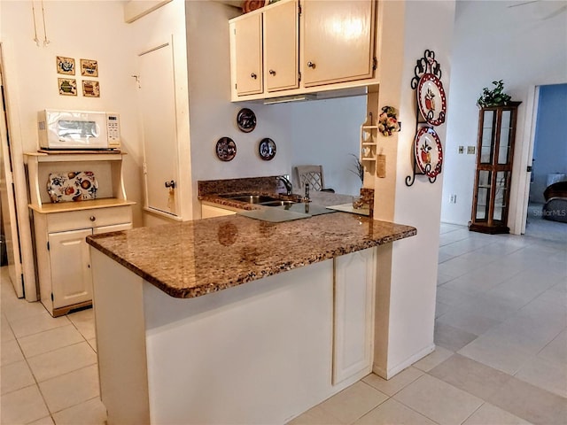 5650 Mashie Cir, North Port, FL 34287 - kitchen featuring white microwave, light tile patterned floors, a sink, a peninsula, and dark stone counters