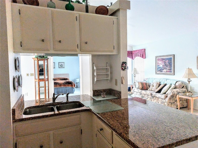 kitchen with cream cabinetry, dark stone countertops, sink, and kitchen peninsula