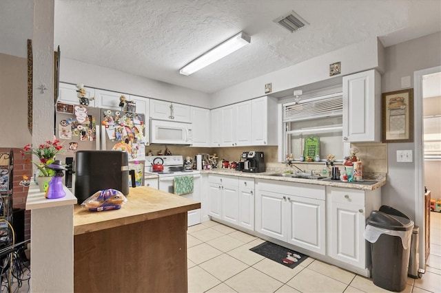 kitchen with white appliances, a textured ceiling, white cabinetry, and light tile patterned floors