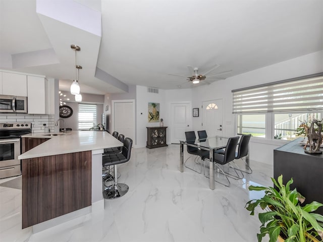 kitchen with a kitchen bar, dark brown cabinets, white cabinetry, appliances with stainless steel finishes, and decorative light fixtures