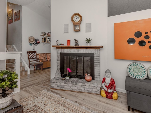 living room with a textured ceiling, a fireplace, light hardwood / wood-style floors, and lofted ceiling