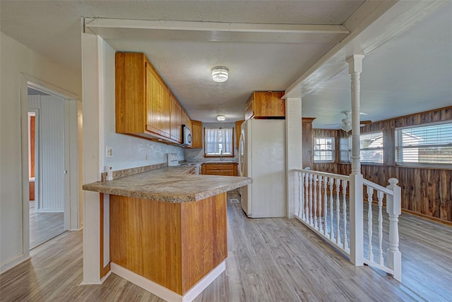 kitchen featuring light hardwood / wood-style floors, kitchen peninsula, wooden walls, and white appliances