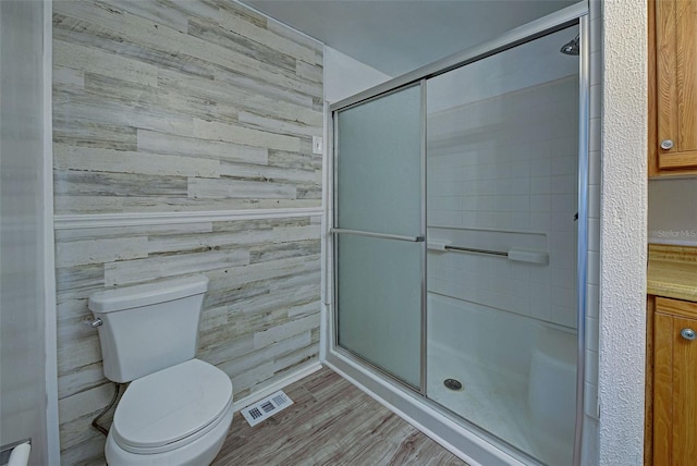 bathroom with toilet, wood walls, hardwood / wood-style flooring, and a shower with door