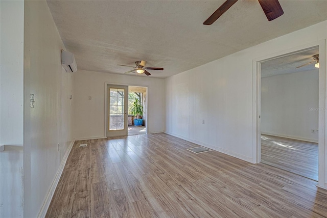 unfurnished room featuring a textured ceiling, an AC wall unit, light wood-type flooring, and ceiling fan