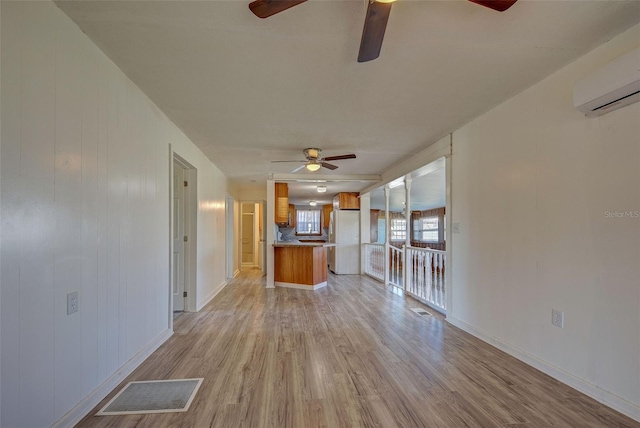 unfurnished living room with light hardwood / wood-style floors, a wall unit AC, wood walls, and ceiling fan