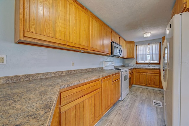 kitchen with white appliances, light hardwood / wood-style floors, a textured ceiling, and sink