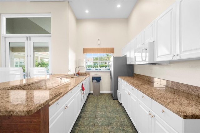 kitchen featuring stainless steel refrigerator, sink, kitchen peninsula, and white cabinets