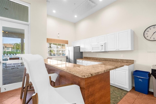 kitchen with stainless steel fridge, white cabinetry, kitchen peninsula, and a healthy amount of sunlight