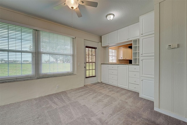 kitchen with a textured ceiling, light colored carpet, white cabinetry, and ceiling fan