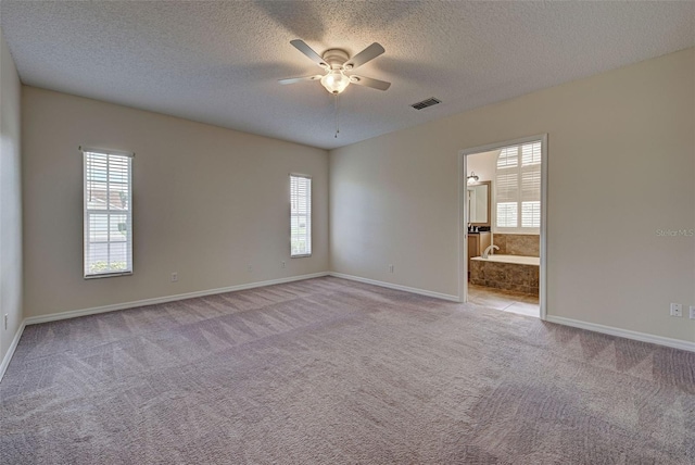 spare room with a textured ceiling, light colored carpet, and ceiling fan