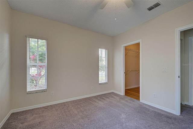 unfurnished bedroom with ceiling fan, a walk in closet, a textured ceiling, and multiple windows