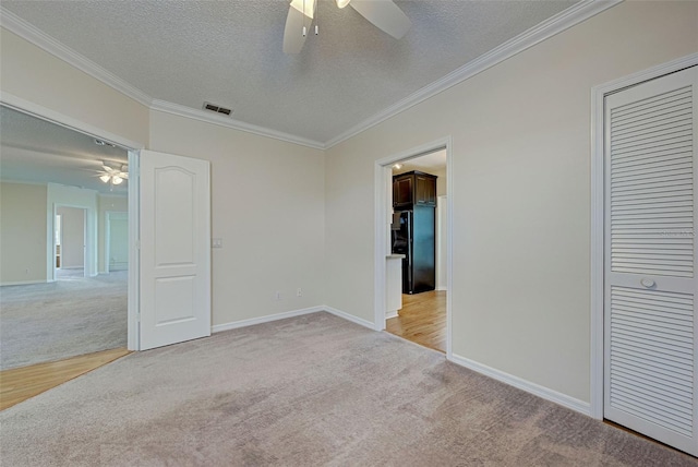 carpeted spare room with ceiling fan, crown molding, and a textured ceiling