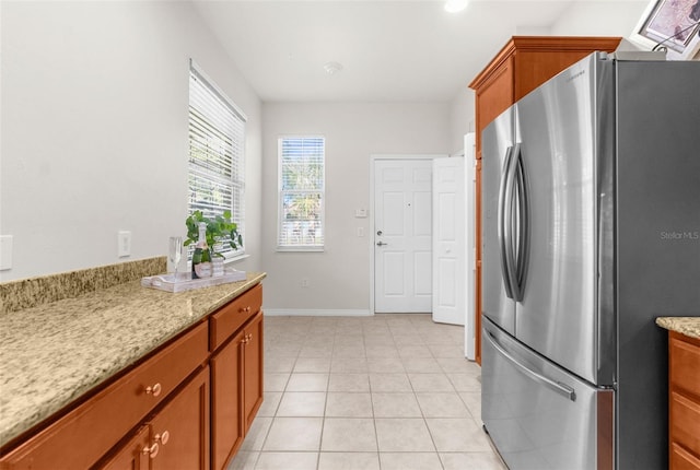 kitchen with stainless steel refrigerator, light tile patterned flooring, and light stone counters