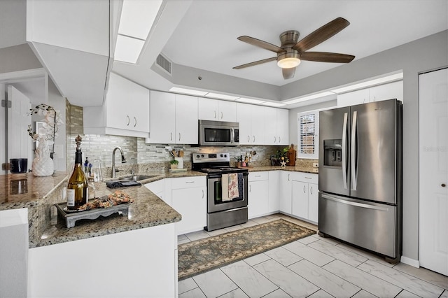 kitchen featuring white cabinetry, sink, stainless steel appliances, kitchen peninsula, and dark stone counters