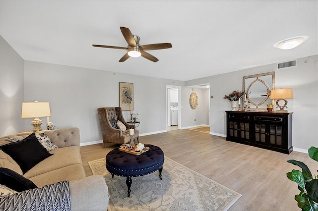 living room featuring washer / clothes dryer, ceiling fan, and light hardwood / wood-style flooring