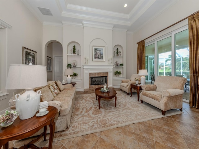 living room with a tiled fireplace, crown molding, built in features, and a raised ceiling