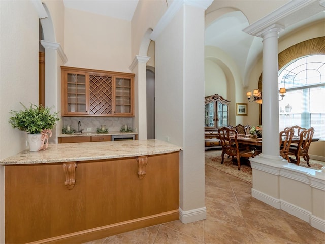 kitchen featuring kitchen peninsula, backsplash, decorative columns, light stone countertops, and light tile patterned flooring