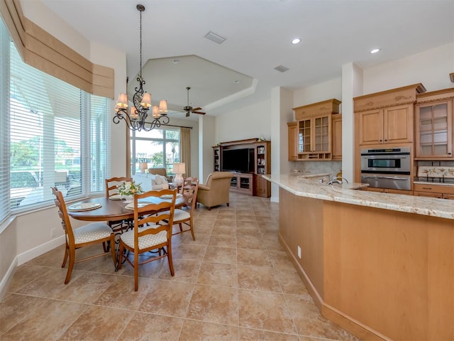 tiled dining area with ceiling fan with notable chandelier and a raised ceiling