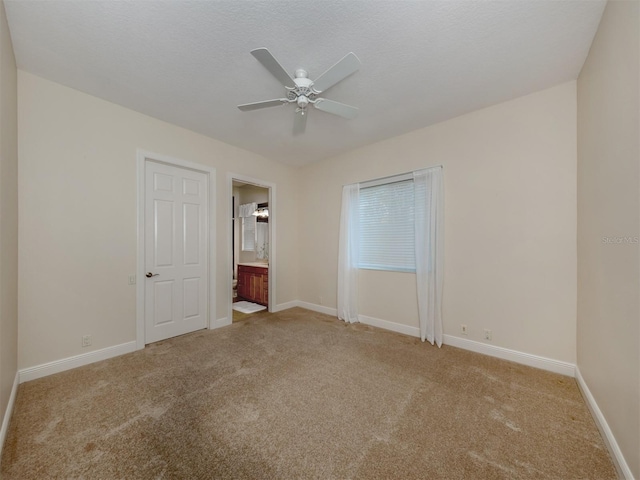 unfurnished bedroom with a textured ceiling, ensuite bathroom, light colored carpet, and ceiling fan