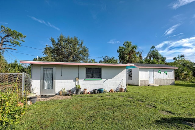 view of front of property with concrete block siding, fence, an outbuilding, and a front yard