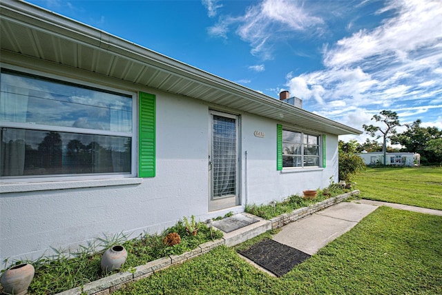 view of exterior entry with a lawn and stucco siding