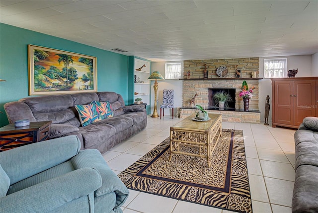 living room featuring a stone fireplace, light tile patterned flooring, and visible vents
