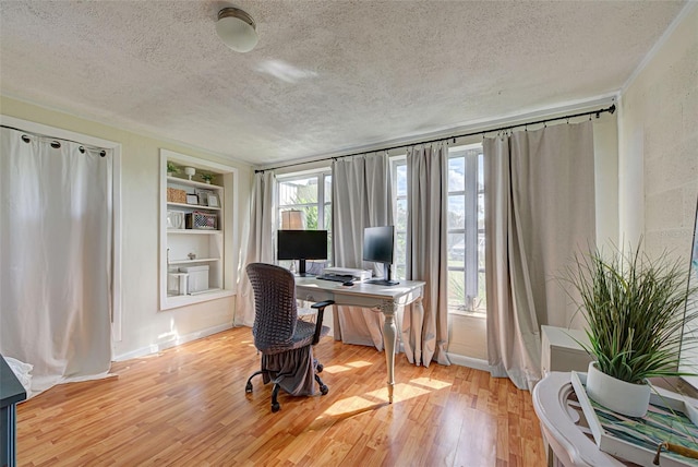 office space featuring a textured ceiling, built in features, baseboards, and light wood finished floors