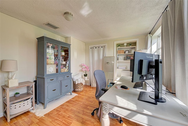 office space with a textured ceiling, visible vents, and light wood-style floors