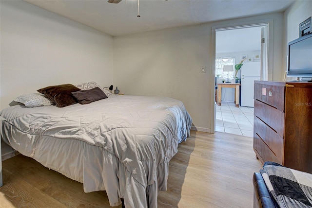 bedroom featuring light hardwood / wood-style flooring, white fridge, and ceiling fan