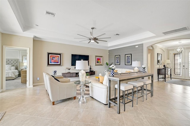 tiled living room featuring crown molding, ceiling fan with notable chandelier, a raised ceiling, and french doors