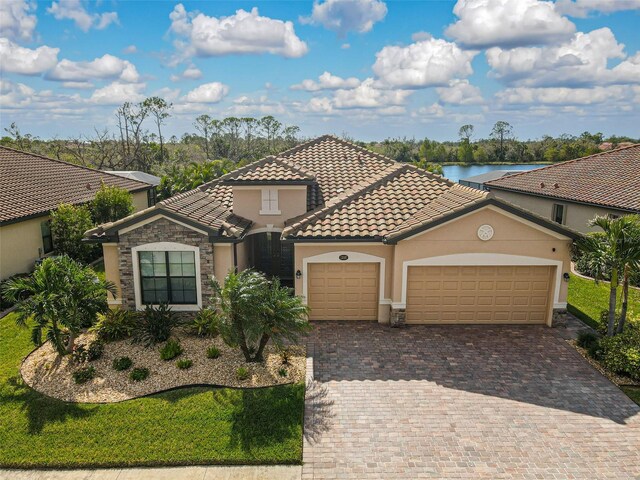 mediterranean / spanish home with a tiled roof, an attached garage, a water view, decorative driveway, and stucco siding