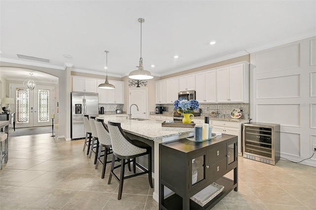 kitchen with arched walkways, a center island with sink, stainless steel appliances, white cabinetry, and a sink