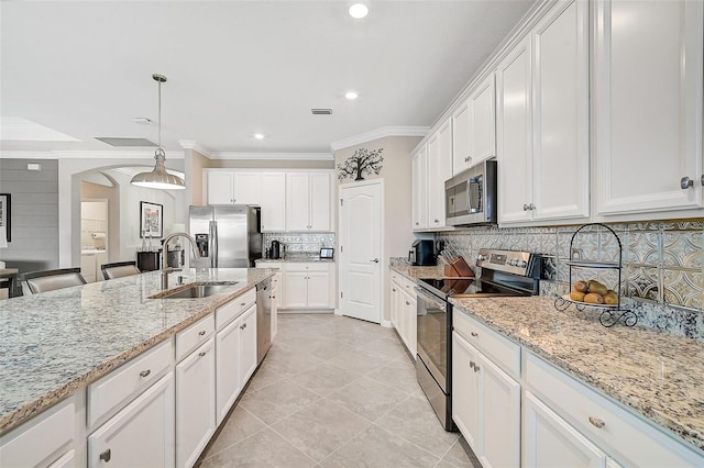 kitchen with a sink, white cabinets, hanging light fixtures, appliances with stainless steel finishes, and light stone countertops