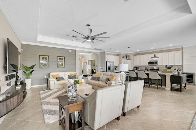 living room with light tile patterned floors, arched walkways, a raised ceiling, a ceiling fan, and crown molding