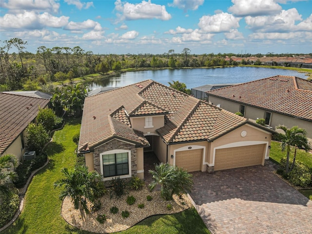 view of front facade featuring stone siding, a tiled roof, a water view, an attached garage, and decorative driveway