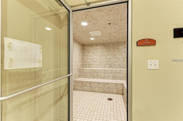 bathroom featuring a textured wall and tiled shower