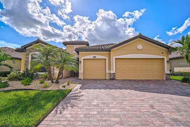 mediterranean / spanish-style home featuring decorative driveway, an attached garage, a tile roof, and stucco siding