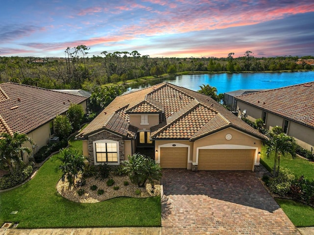 mediterranean / spanish-style home with decorative driveway, a tile roof, stucco siding, a water view, and a garage