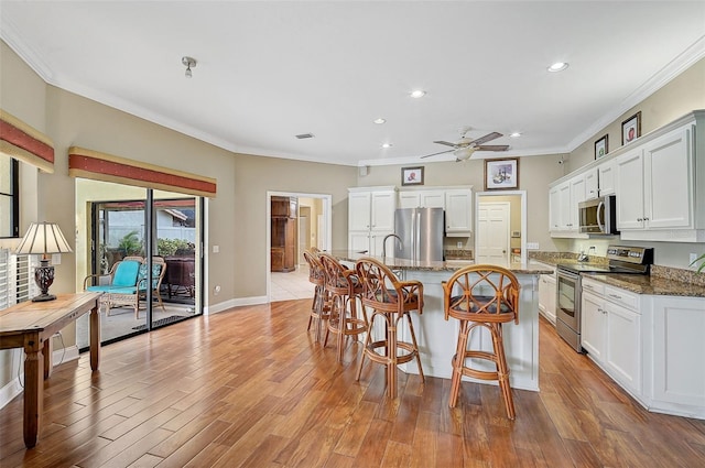 kitchen with dark stone countertops, white cabinets, stainless steel appliances, and light hardwood / wood-style floors