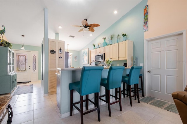 kitchen with light tile patterned floors, high vaulted ceiling, a breakfast bar, and decorative light fixtures