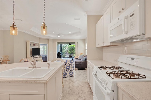 kitchen featuring hanging light fixtures, a tray ceiling, a center island with sink, sink, and white appliances