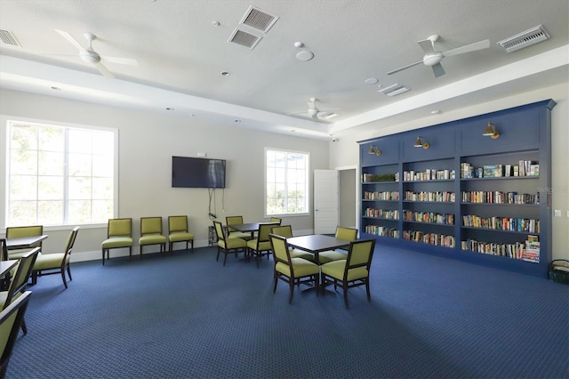 rec room with ceiling fan, a tray ceiling, and dark colored carpet