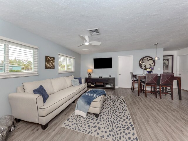 living room featuring ceiling fan, a textured ceiling, and light hardwood / wood-style flooring