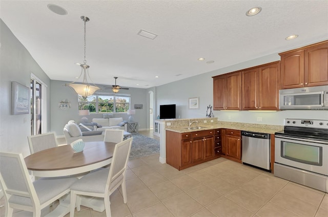 kitchen with kitchen peninsula, light stone countertops, stainless steel appliances, sink, and decorative light fixtures