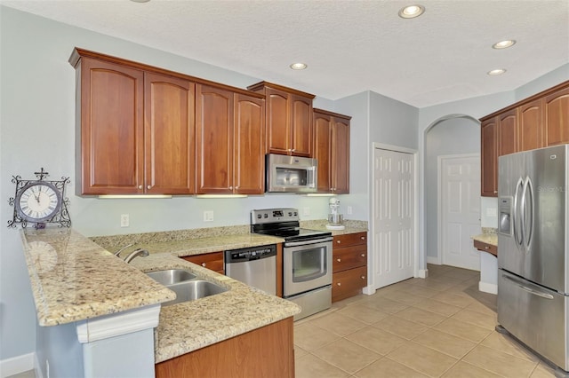 kitchen with kitchen peninsula, stainless steel appliances, sink, light stone counters, and a textured ceiling